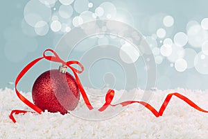 Red Christmas ball with a scarlet satin bow in the snow on a blue background with bokeh lights. happy new year card