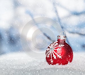 Red Christmas ball on snow against snowing winter landscape.