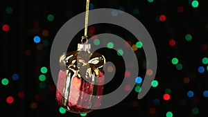 Red Christmas ball swinging on defocused background with flashing garland lights.