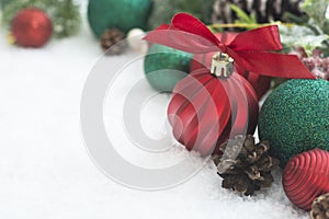 Red Christmas balls, baubles with ribbon and green fir branches, pine cones, on white snow background. Winter holidays