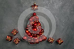 Red Christmas balls lie in the shape of a Christmas tree on a gray background. Gifts next to the tree. Christmas card. Flat lay,