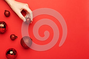 Red Christmas balls on a red background top view. A female hand holds a festive New Year`s decor, flat lay. Xmas winter