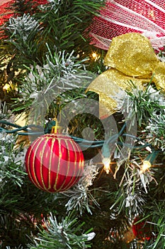 Red christmas bauble and gold ribbon in a tree with light decorations