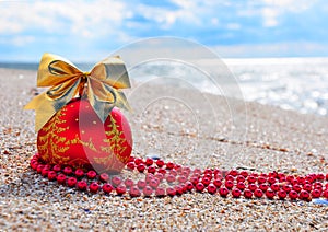 Red christmas bauble with golden bow on the sand
