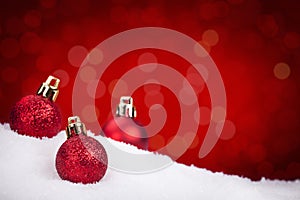 Red Christmas baubles on snow with a red background