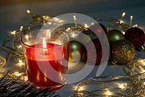 Red christmas candle, burning candle fire on a table with holiday garland and pine tree decorations and balls, festive