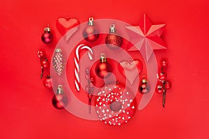 Red Christmas composition with red holly berries, Xmas candy, baubles and star on colorful red background. Xmas flat lay top view