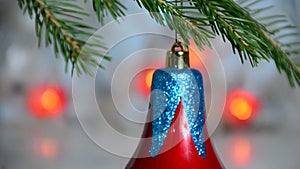 Red Christmas decor ball on green tree branch of a Christmas tree on a background of Christmas lights new year