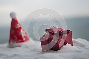 Red Christmas gift box and fir tree on snow. Christmas home decoration with snow and tree on blurred background at daytime with co