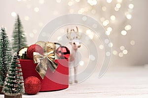 Red Christmas gift box with a gold bow on the background of bokeh, Christmas trees and deer