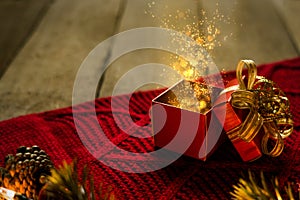 Red Christmas gift box on red scraf with gold particles light magical on wooden desk