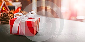 Red christmas gift box with white ribbon on table against bokeh background