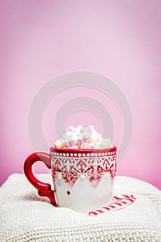 Red Christmas mug with marshmallows, sugar cane on a cozy sweaters and pink background