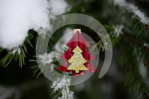 Red Christmas ornament in shape of fir tree on snow-covered Christmas tree branch outdoors