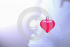 Red christmas ornaments heart, on the white xmas tree on blurry background. Merry christmas card. Winter holiday theme. Happy New