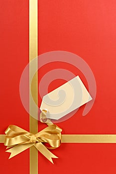 Red Christmas paper background, gold gift ribbon bow, blank gift tag vertical