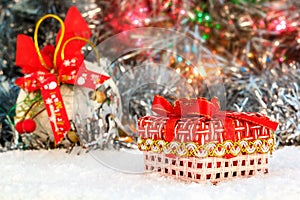 Red Christmas present stands on the snow against a background of a Christmas ball and shiny tinsel. glowing lights. bokeh