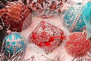 Red Christmas present stands on the snow against a background of a Christmas balls and shiny tinsel