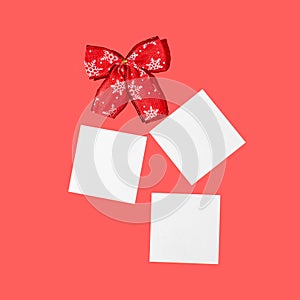 Red Christmas ribbon bow and white square paper on red background. Christmas or New year card idea. Winter holiday concept. Copy