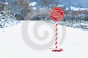 Red Christmas sign with text \'Santa Stop here\' in snowy landscape