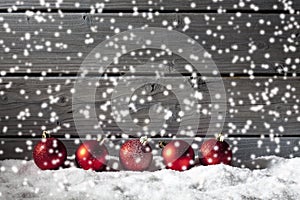 Red christmas spheres on pile of snow against wooden wall
