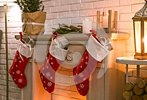 Red Christmas stockings with gifts on decorative fireplace. Festive interior