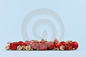 Red Christmas tree baubles, small gift boxes and golden stars and bells arranged in a row at bottom of blue background