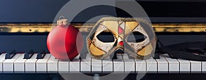 Red Chritmas ball and carnival mask on piano keyboard, front view