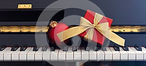 Red Chritmas ball and gift box on piano keyboard, front view