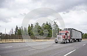 Red classic big rig semi truck tractor with vertical pipes and chrome accessories transporting cargo in covered bulk semi trailer