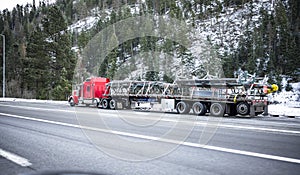 Red classic powerful big rig semi truck transporting oversized industrial cargo on long flat bed semi trailer running on the