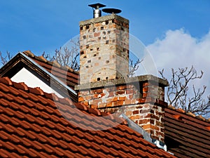 Red clay roof detail with brick chimneys under blue sky