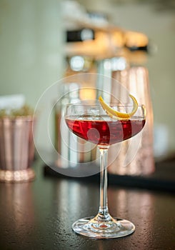 Red clear drink in vintage champagne glass with orange zest decoration on a bar table