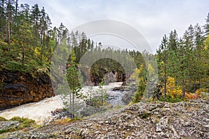 Red cliff, stone wall, forest, waterfall and wild river view in autumn