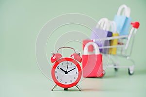 Red clock with blurred shopping cart and multi color shopping bags on green background, sales ,promotion ,advertisements