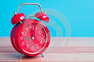 Red clock placed on wooden table on blue background