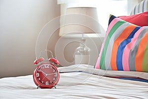 Red clock on white blanket and colorful striped pillows