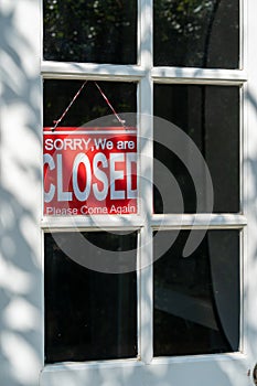 Red closed sign hanging on the white entrance door of a business office