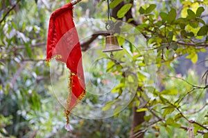 a red cloth and a bronze bell tied to a branch by a shrine photo