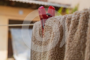 A red clothespin fixes a brown towel on a clothesline against the background of a blurred wall of a building on a sunny photo