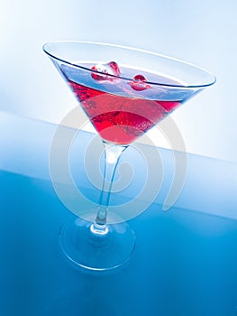 Red cocktail drink with ice cubes on blue light tint background, fun and dance disco