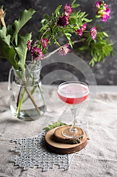Red cocktail with foam in margarita glass and flowers on the table