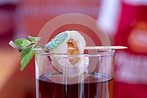 Red cocktail in a glass with a skewer of shrimp and mint, closeup