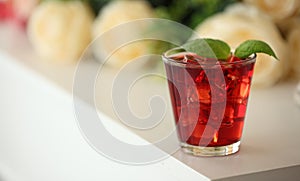 Red cocktail with ice, decorated with mint leaf on light background