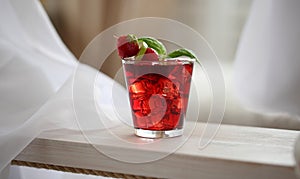 Red cocktail with ice, decorated with mint leaf, lime and trawberry on light background