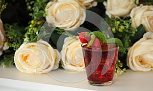 Red cocktail with mint leaf, lime and strawberry, roses on background