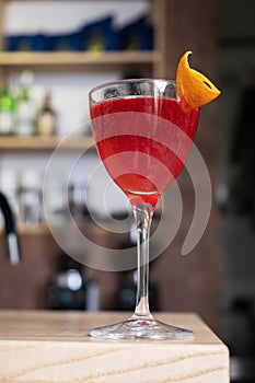 Red cocktail with orange decoration in a glass on a wooden bar table