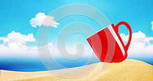 Red coffee cup on beach sand over blurry blue sky with clouds an