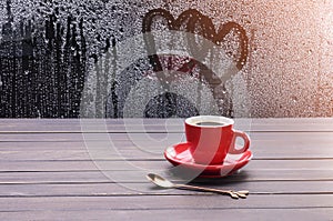 Red coffee cup with black coffee Placed on an old vintage wooden table by the window with raindrops and hearts on the glass floor