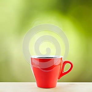 A red coffee cup with steaming on wood desk with top copy space and green nature background refreshment breakfast